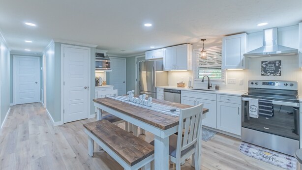 A modern kitchen with white cabinets, a wooden dining table, and stainless steel appliances.