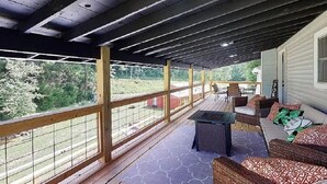 A covered porch with a wooden railing, a seating area with a table and chairs, and a view of the surrounding landscape.