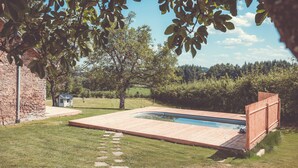 A swimming pool with a wooden deck, surrounded by a grassy lawn and trees. - House in the heart of the Périgord Vert. (Payzac)