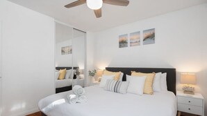 A modern bedroom with a large bed, bedside tables, a ceiling fan, and wall art.