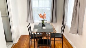 A dining area with a wooden table, six chairs, a vase with flowers, and a window with curtains.