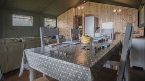 A cozy cabin interior with a dining table, chairs, a sofa, and a kitchen area with a refrigerator and cabinets.