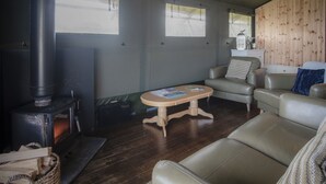 A cozy living room with a wood-burning stove, leather sofas, a wooden coffee table, and a view through the windows.