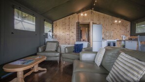 A cozy living area with a sofa, armchairs, a wooden coffee table, and a kitchen in the background.