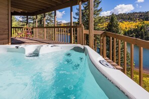 Een hottub op een houten terras met uitzicht op een meer en herfstkleurige bomen.
