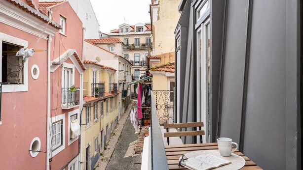 A narrow street with buildings on either side, a balcony with a table and a mug, and clothes hanging on a line. - Studios Terra & Mar (Lisbon)