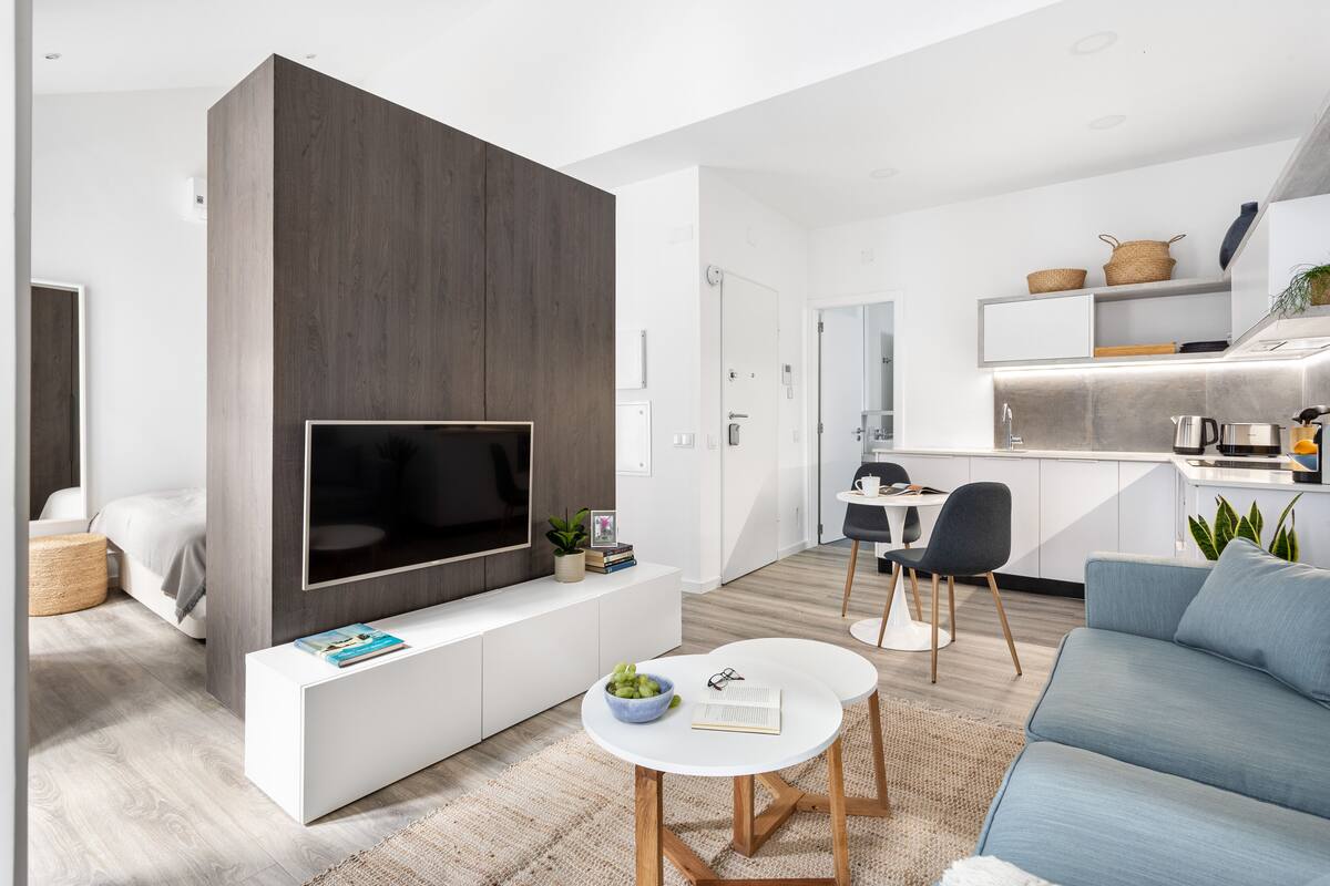 Un salon moderne doté d’un grand téléviseur à écran plat, d’un canapé, d’une table basse et d’un coin repas comprenant une chaise et une petite table.