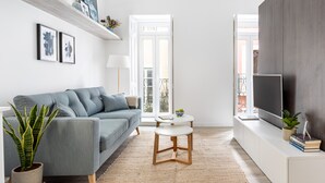 A modern living room with a grey sofa, a round white coffee table, and a flat-screen TV on a white console. - Studios Terra & Mar (Lisbon)