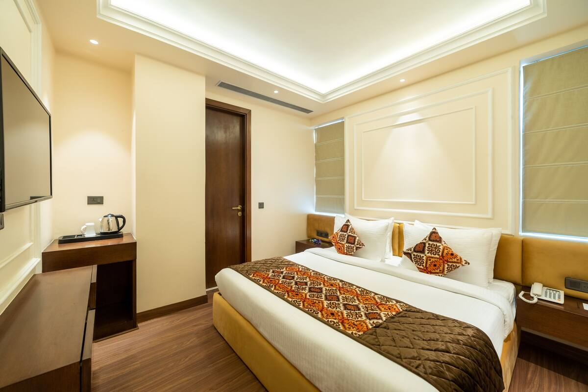 A hotel room with a large bed, a bedside table with a phone, a flat-screen TV, and a door.