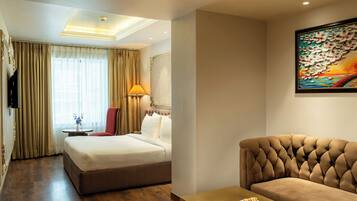 Habitación de hotel con cama, sofá, mesa con bandeja de comida, lámpara y un cuadro en la pared.