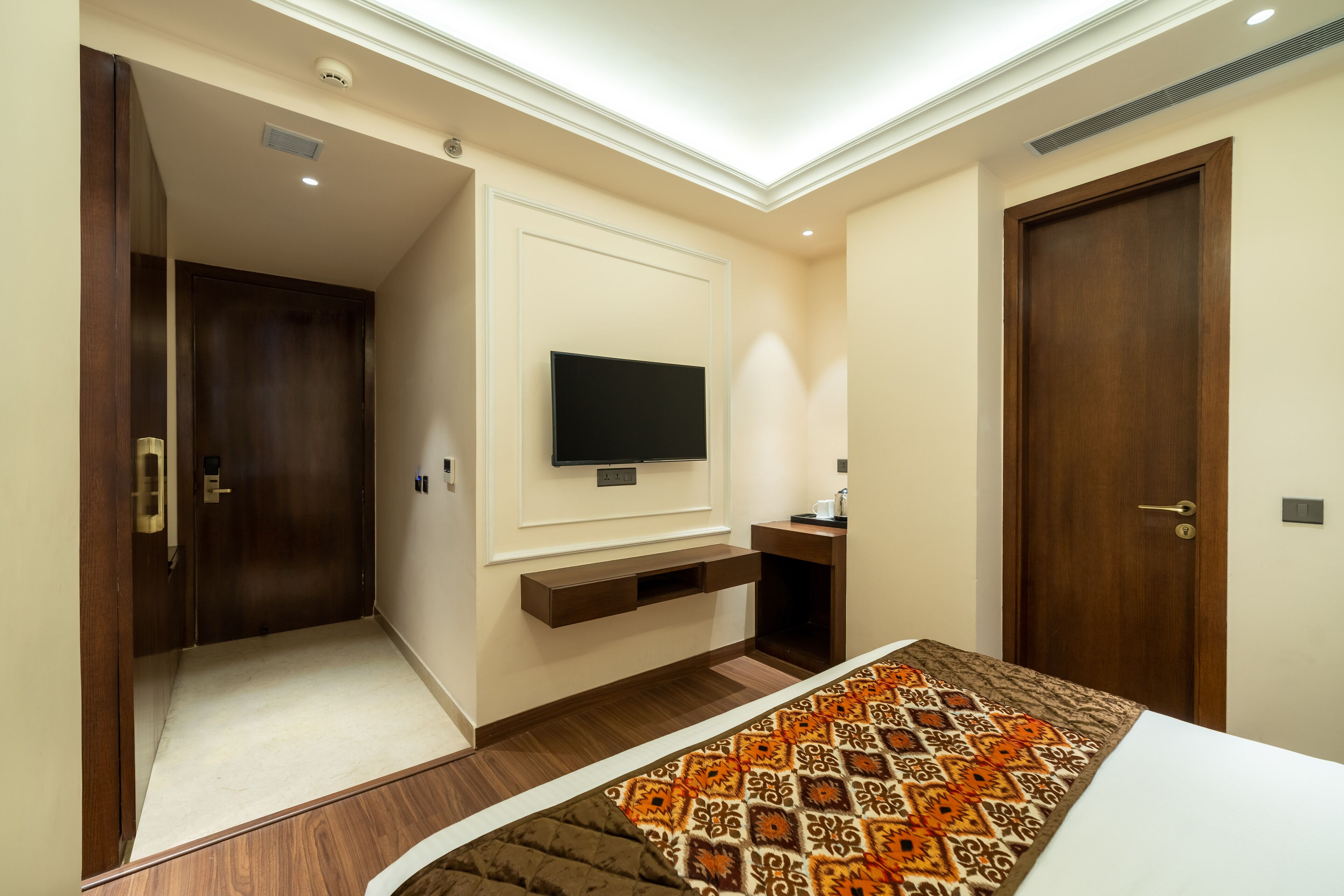 Un dormitorio con una televisión montada en la pared, una cama con colcha estampada y una puerta de madera.