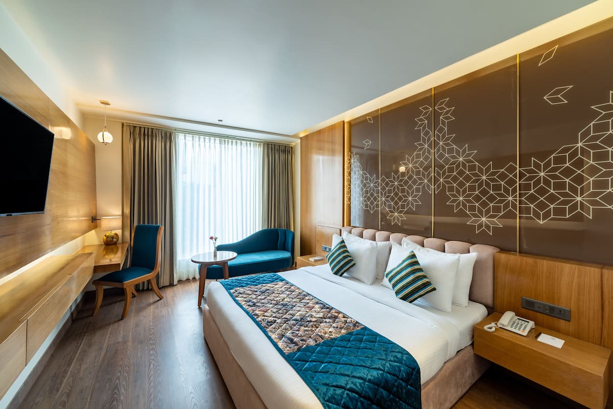 A modern hotel room with a large bed, a desk, a chair, and a TV.