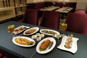 A dining table with various dishes and drinks, set in a restaurant with red upholstered chairs and a dark tablecloth.