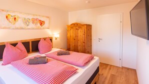 Camera d'albergo con due letti, lenzuola a quadri, un armadio in legno, una TV a parete e un'opera d'arte a tema cuore.