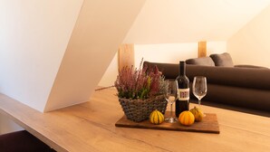 Un tavolo in legno con un cesto intrecciato contenente piante essiccate, due bottiglie di vino e due bicchieri da vino. Si vede anche una piccola zucca sul tavolo.