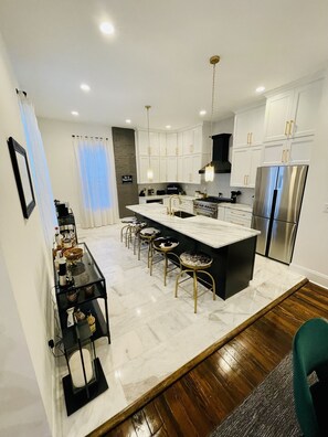 Una cocina moderna con armarios blancos, electrodomésticos de acero inoxidable y una isla de mármol con taburetes de bar.