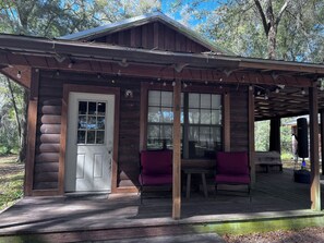 Cozy cabin with a porch, featuring a white door, wooden window frame, and small table with bench.