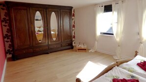 A bedroom with a wooden wardrobe, a bed with a floral bedspread, and a window with curtains.