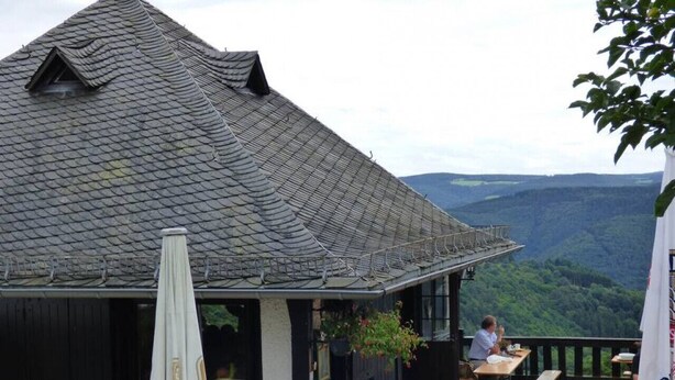 An outdoor dining area with tables and benches, a covered seating area, and a view of the surrounding landscape.