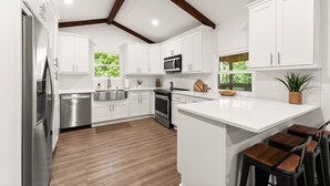 A modern kitchen with white cabinets, stainless steel appliances, and a wooden floor. - Private Dock | Hot Tub | Kayaks | GameRoom | EV (Dawsonville)
