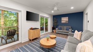 A modern living room with a grey sofa, a wooden coffee table, a blue-striped rug, a wooden cabinet, and a flat-screen TV mounted on the wall. - Private Dock | Hot Tub | Kayaks | GameRoom | EV (Dawsonville)