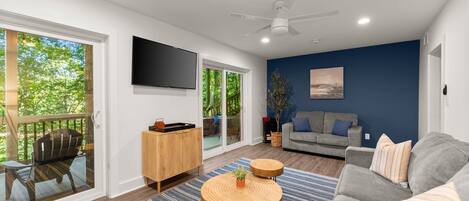 A modern living room with a grey sofa, a wooden coffee table, a blue-striped rug, a wooden cabinet, and a flat-screen TV mounted on the wall.