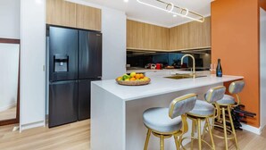 A modern kitchen with a central island, black refrigerator, and bar stools. - Top Floor in Burleigh: Pool Parking Walk To Beach (Gold Coast)