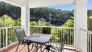 A balcony with a table and chairs, overlooking a lush green landscape with trees and a power line. - Top Floor in Burleigh: Pool Parking Walk To Beach (Gold Coast)