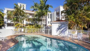 A swimming pool with a wooden deck, surrounded by palm trees and white railings. - Top Floor in Burleigh: Pool Parking Walk To Beach (Gold Coast)
