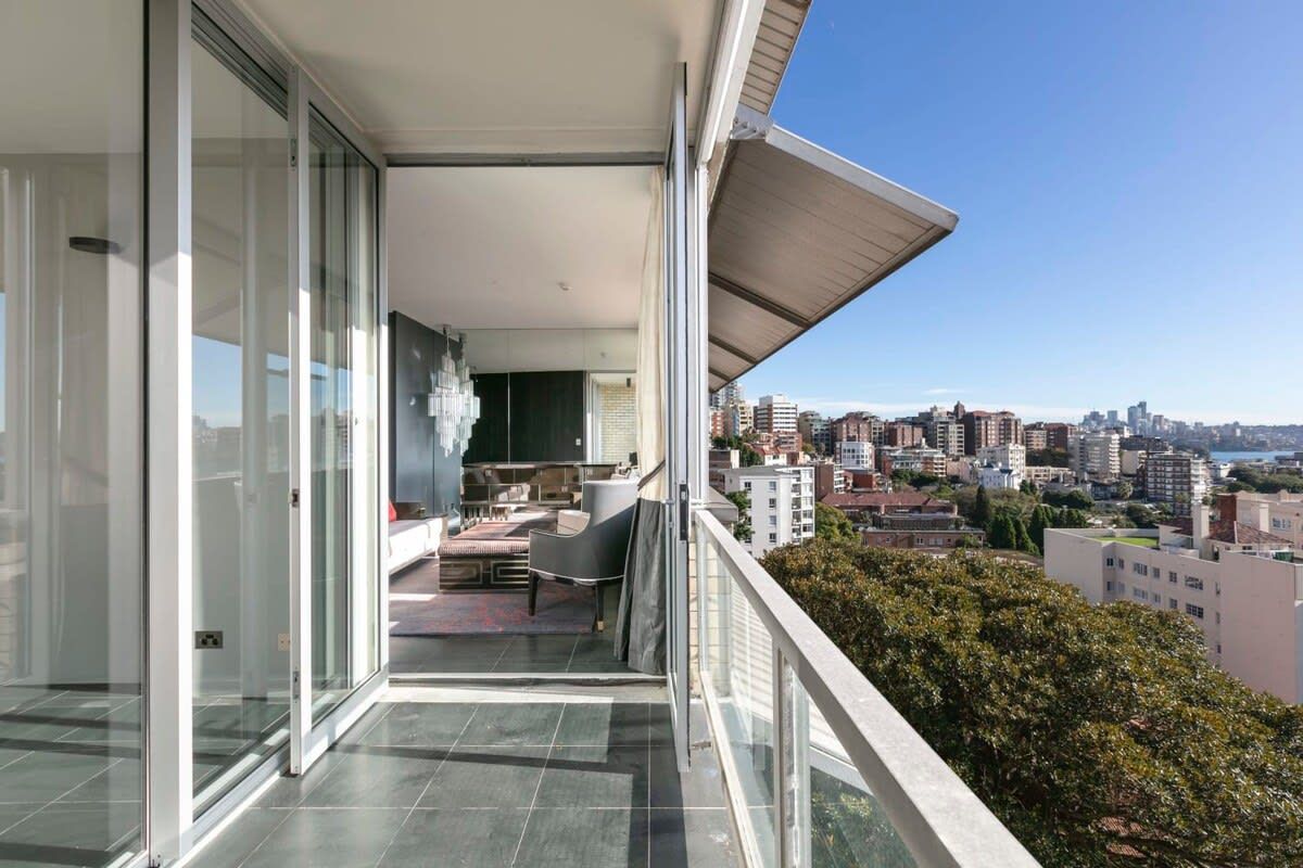 Un balcón con vistas a la ciudad, una puerta corredera de vidrio y una zona de estar con una mesa y sillas.