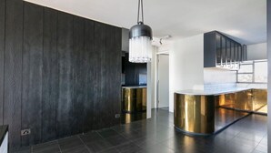 Eine moderne Küche mit dunklen Holzpaneelen, einer zentralen Kochinsel mit goldenen Akzenten und einer Pendelleuchte.