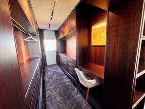 A narrow walk-through closet with wooden cabinets, a grey carpet, and a white chair. - Luxury 1 Bedroom Apt with Harbour Views & Parking (Sydney)