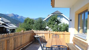 Una terraza de madera con mesa y sillas, una valla de madera y vistas a la montaña.