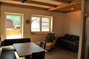 A room with a dining table, a sofa, a chair, and two windows.