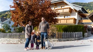 Una familia parada frente a una casa con un muro de piedra y una valla de madera.
