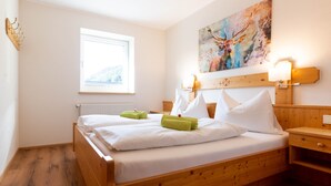 Una cama de madera con ropa de cama blanca y toallas verdes, una ventana con vistas, y un cuadro de un ciervo en la pared.