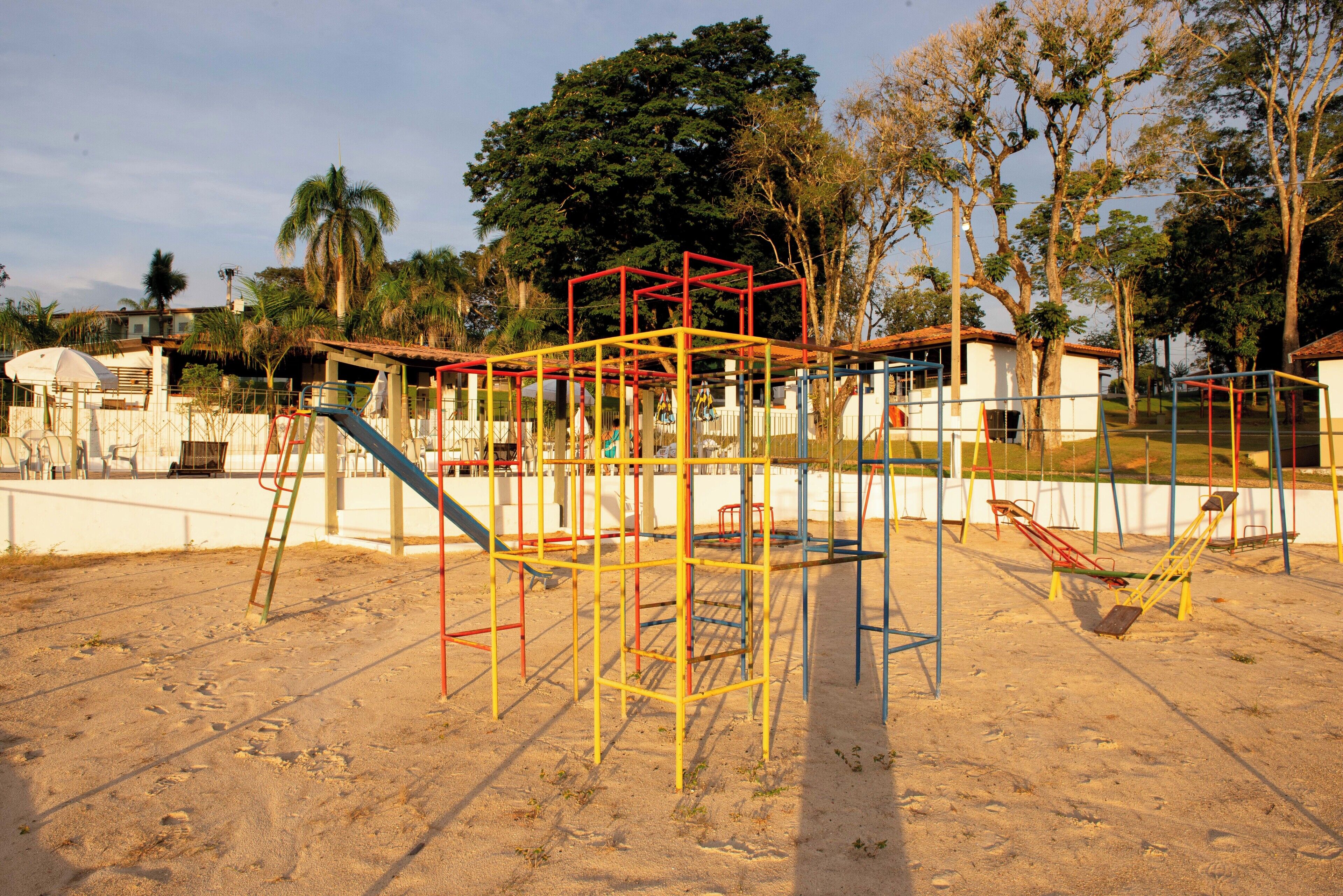 A playground with various play structures, including slides and swings, surrounded by sand and trees.