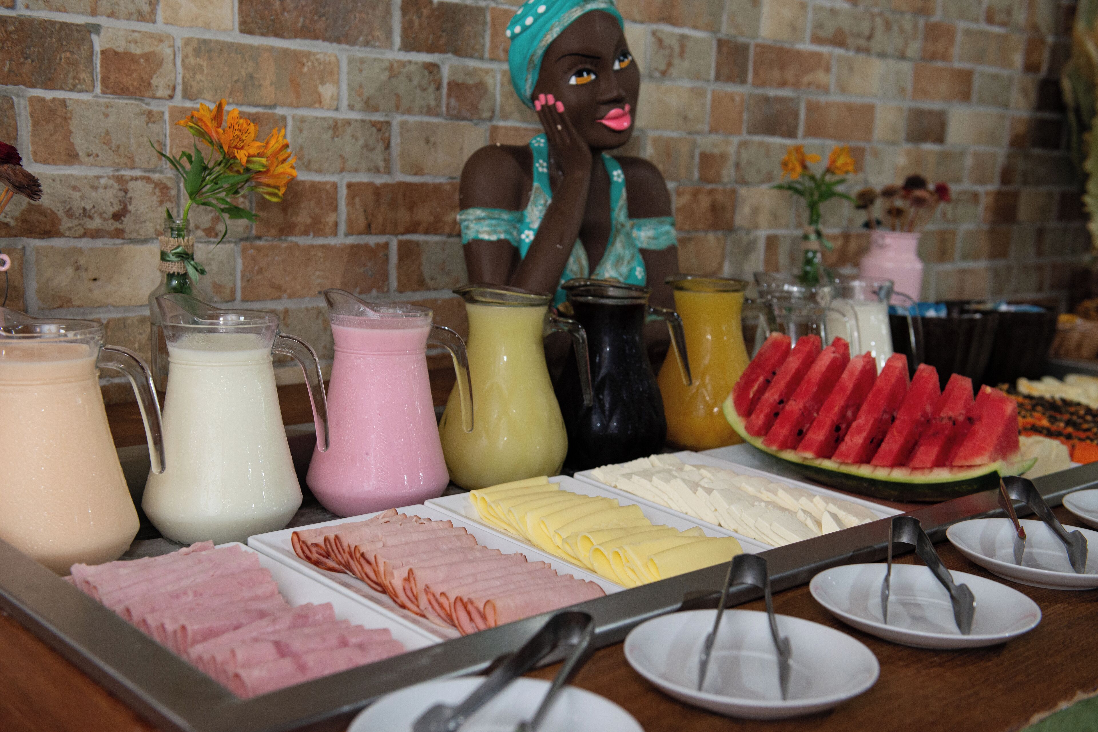 A buffet table with various food items and drinks, including sliced meats, cheeses, and a watermelon.