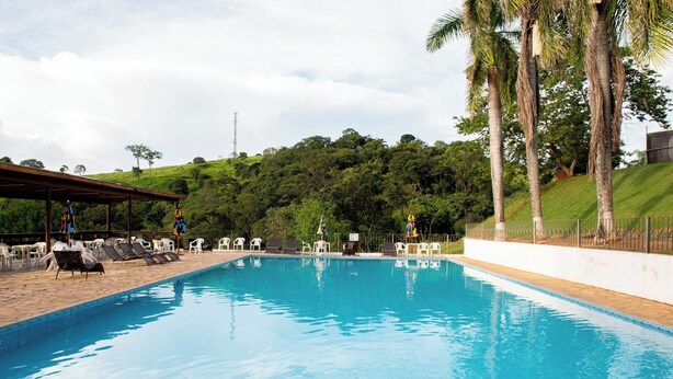 Una piscina con sillas de descanso y una zona cubierta, rodeada de follaje y palmeras.