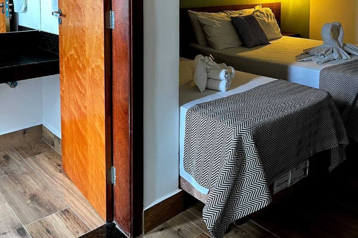 Habitación de hotel con puerta de madera, cama con colcha estampada, mesita de noche y una pared decorada con platos.
