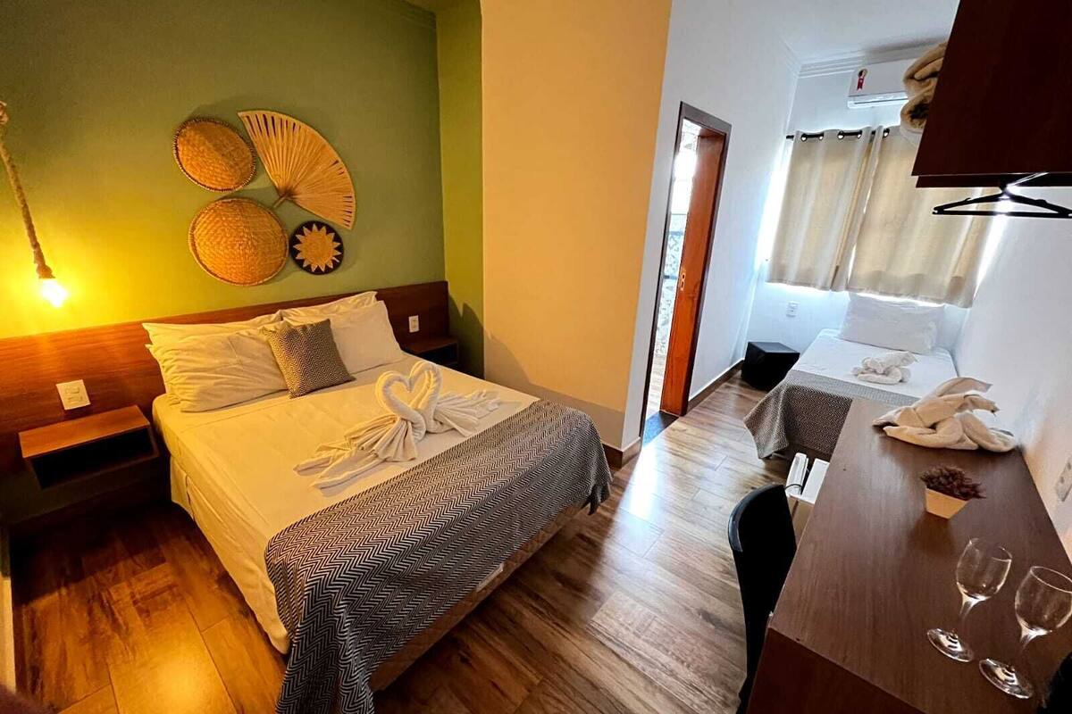 Habitación de hotel con cama, mesitas de noche, escritorio con silla, espejo y ventana con cortinas.