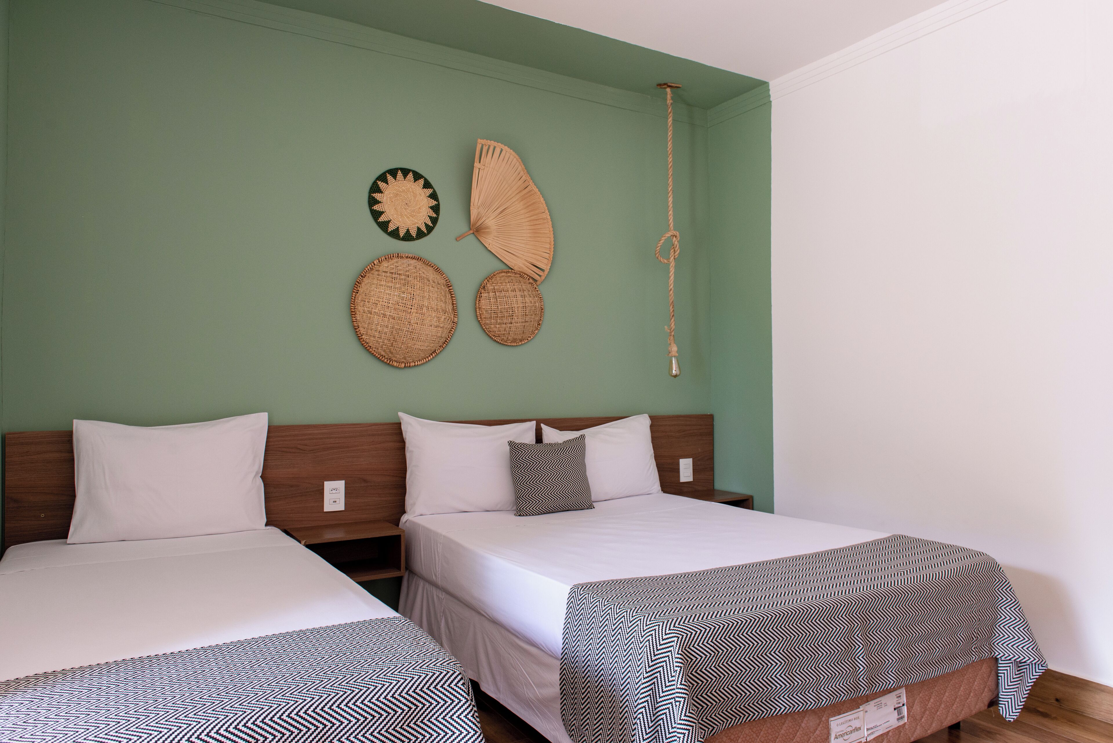 A room with two beds, a green wall, and three woven wall hangings.