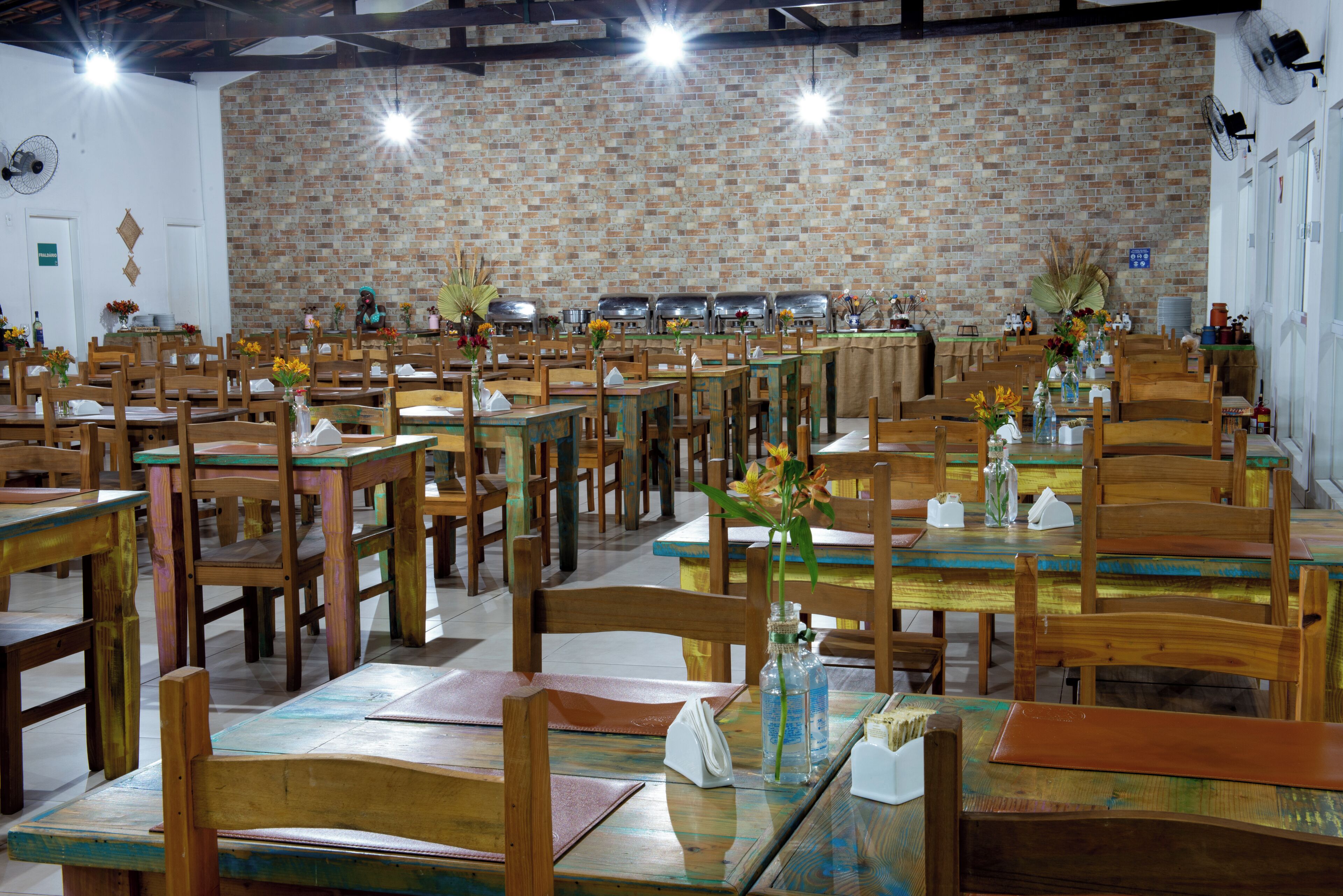 Un restaurant doté de nombreuses tables et chaises en bois, de murs en briques et d’un plafond également en briques.