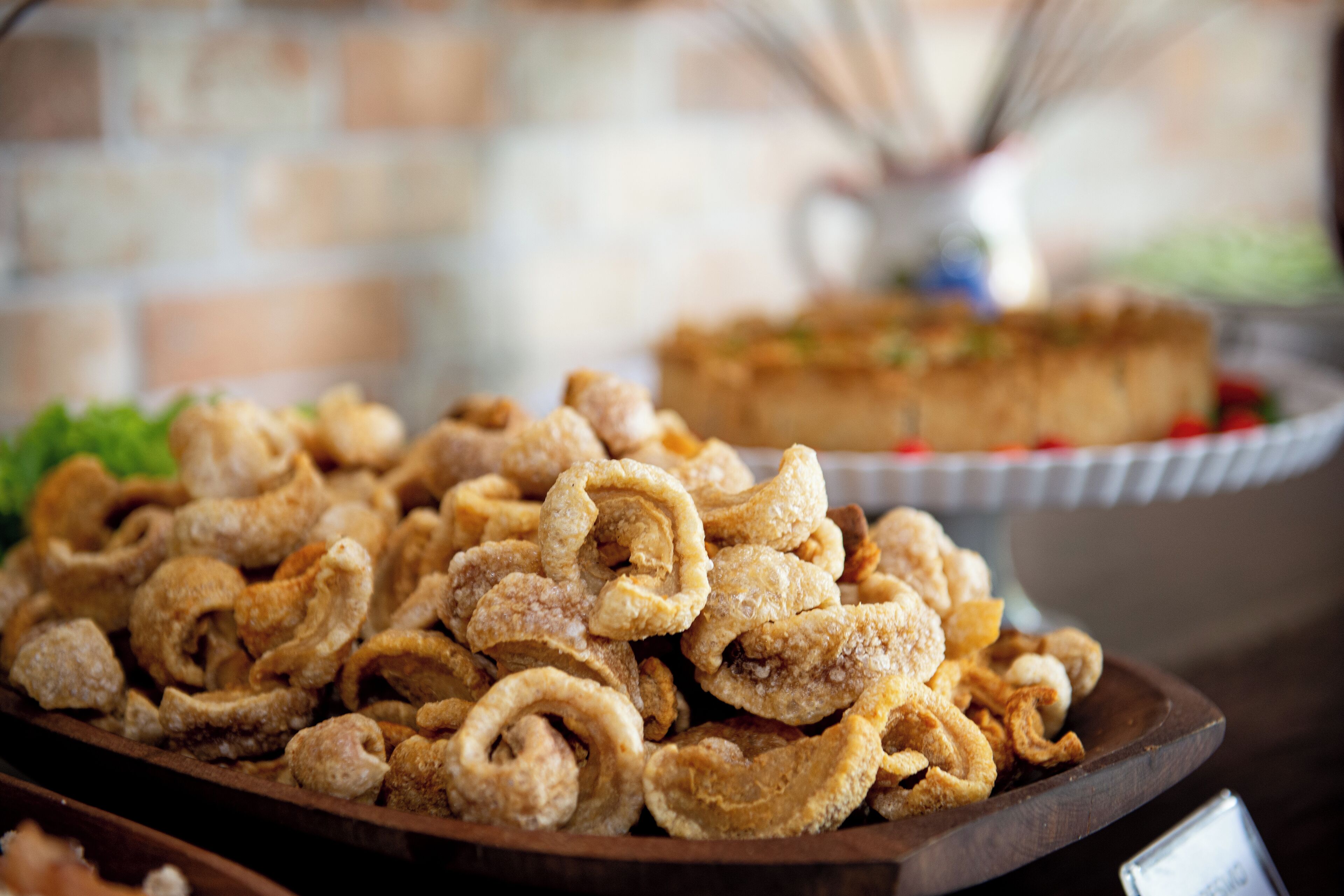 A wooden serving tray filled with fried snacks, a pie on a white plate, and a blurred background with a brick wall.