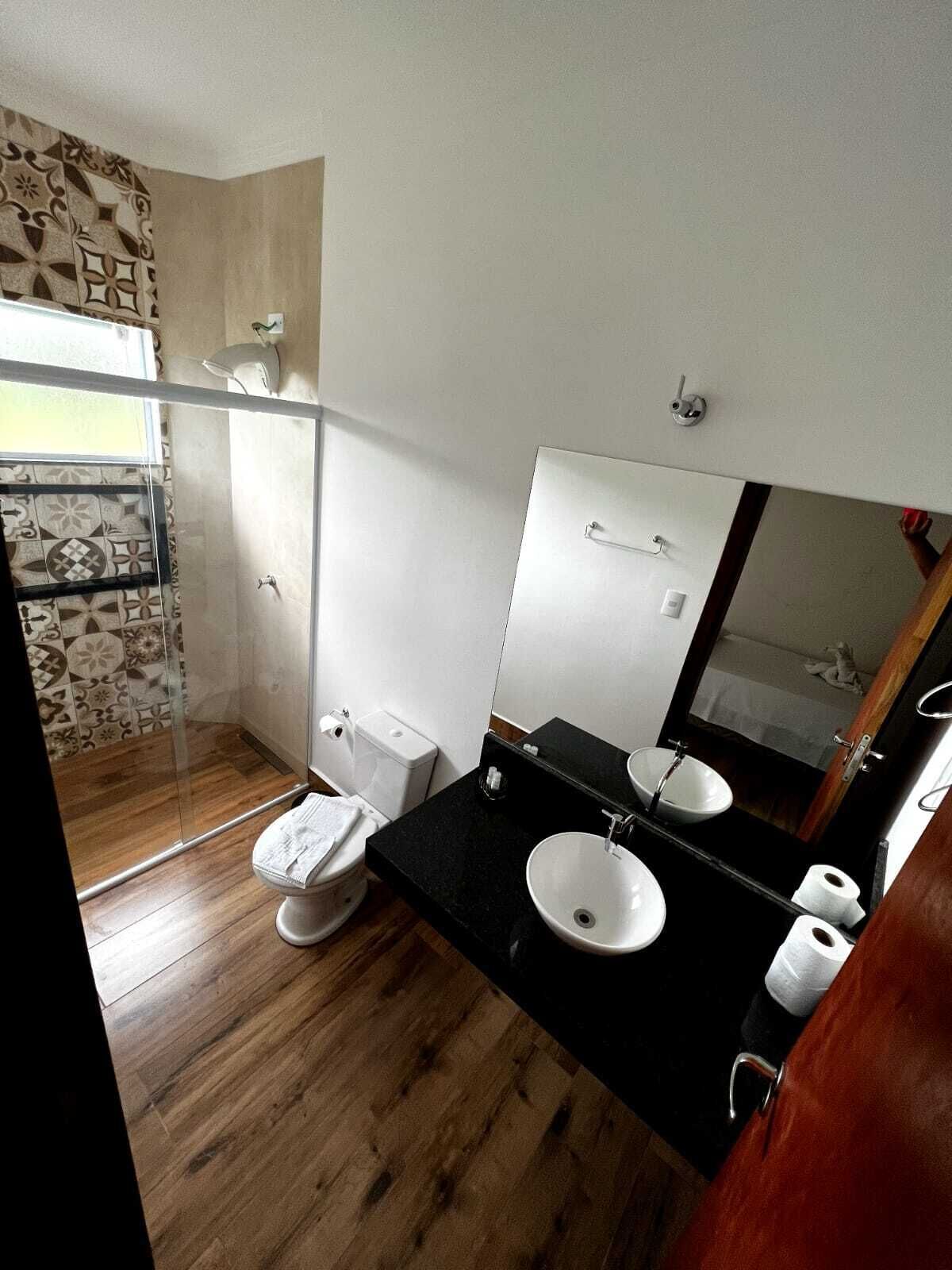 Et badeværelse med trægulv, hvid toilet, sort vask og et stort spejl.