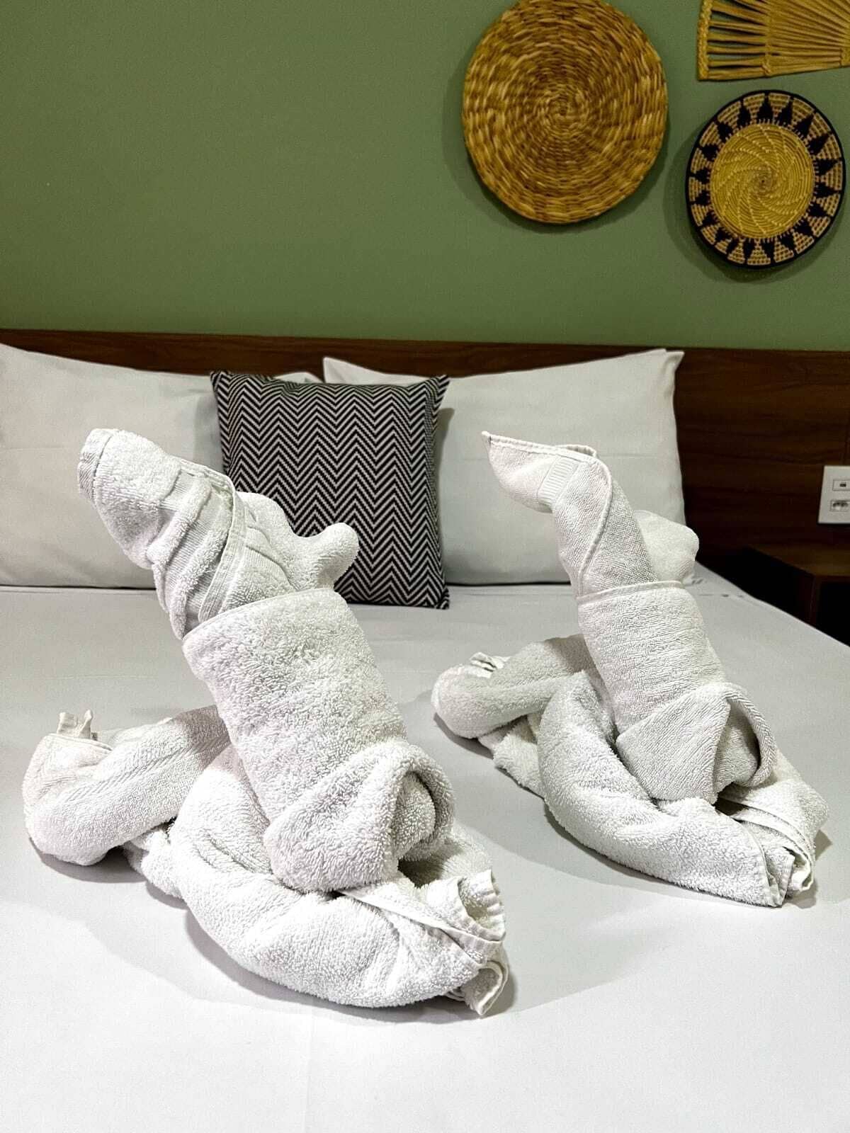 A bed with two towels arranged in a playful manner, a wooden headboard, and two decorative pillows.