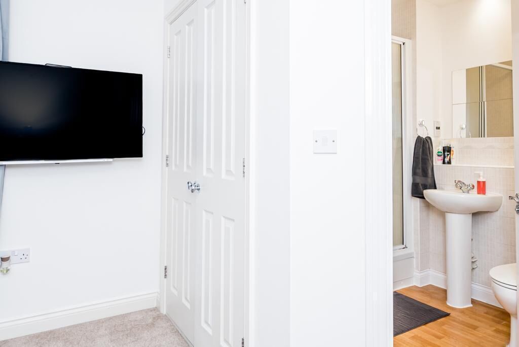 Una stanza con TV a schermo piatto montata al muro, una porta bianca e un bagno con lavandino, specchio e water.