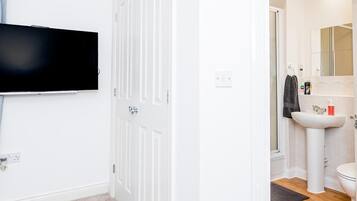 Una stanza con TV a schermo piatto montata al muro, una porta bianca e un bagno con lavandino, specchio e water.