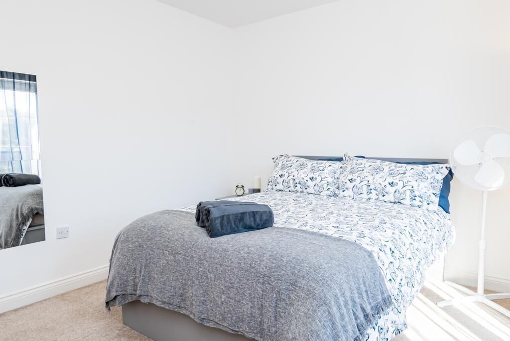 Une chambre à coucher avec un lit, une table de chevet, un miroir et une fenêtre avec des rideaux.