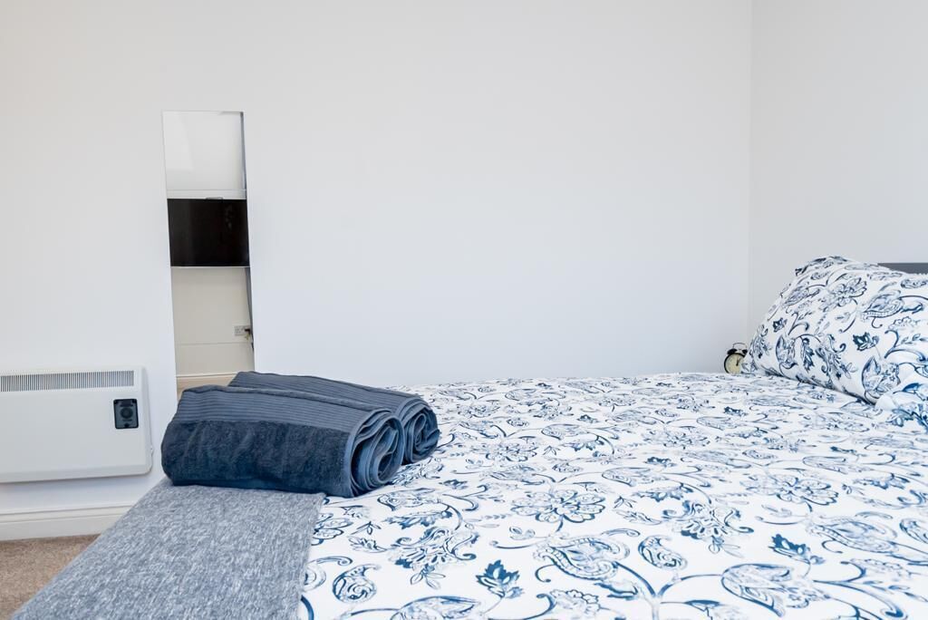 Ein ordentlich bezogenes Bett mit einer blau-weißen blumigen Tagesdecke, einer aufgerollten grauen Decke und einer grauen Wolldecke auf einer hölzernen Bank.